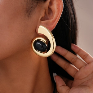 Close-up of golden spiral earrings with black oval gemstones on model's ear