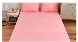Close-up of pink fitted bed sheet and matching envelope pillowcases on a wooden bed