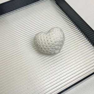 Close-up of a white handmade knitted heart brooch with detailed crochet texture on a tray