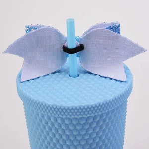 Blue glitter bow straw topper accessory with elastic band on a textured tumbler