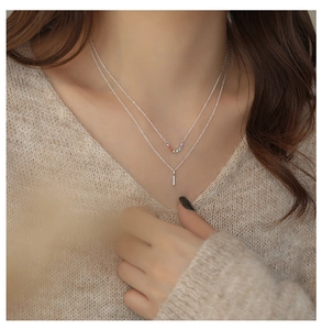 Detail of layered silver necklace with rainbow stones and a zircon bar pendant on model