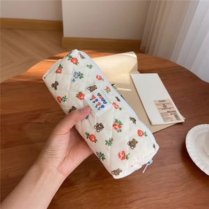 Hand holding a cream quilted pencil case with floral and bear patterns on wood desk