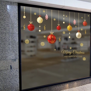 Détail de stickers de Noël avec boules suspendues, flocons et lettrage festif doré sur vitre