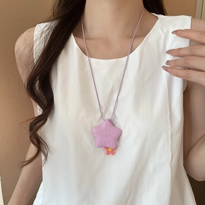 Dettaglio del ciondolo a stella viola con testo a rilievo e fiore su camicia bianca