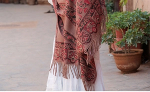 Dettaglio della stampa paisley etnica e frange con nappe su uno scialle rosso in stile cashmere