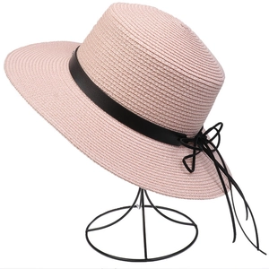 Detail of pink straw sun hat with black ribbon and bow on a black metal mesh stand