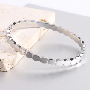 Polished silver hexagonal honeycomb bangle bracelet displayed on a white marble stone base