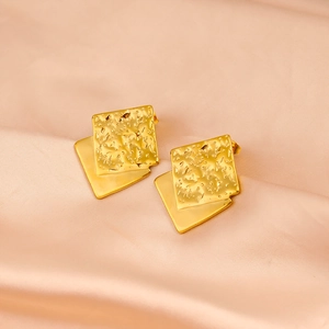 Macro view of gold stainless steel square earrings with hammered texture on pink silk fabric