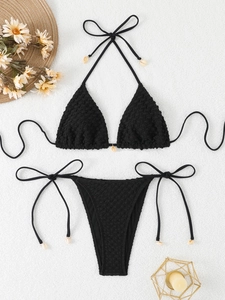 Detail of black textured bikini set with hanging shell charms on flat lay display