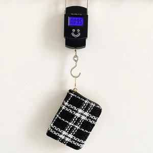 Lightweight black and white plaid tweed small coin purse with gold zipper shown on a scale