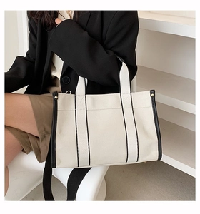 Detail of canvas tote bag with black leather trim and reinforced gold metal rivets