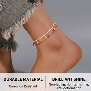 Detail of double-layer stainless steel anklet with white beads and daisy charm on beach