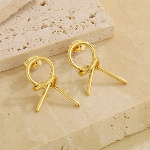 Macro shot of minimalist gold knotted hoop earrings on natural stone background