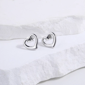 Detailed view of silver heart-shaped stud earrings on white textured stone background