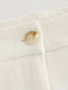 Macro shot of natural beige button on white linen blend fabric waist detail