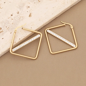 Detailed view of square gold earrings with diagonal rhinestone inlay on stone surface