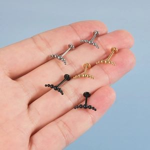 Detailed close-up of curved labret studs in silver, gold and black finishes held by hand