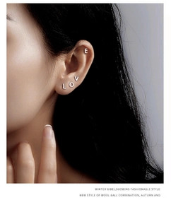 Detail view of L O V E letter silver studs worn on the ear for a minimal look