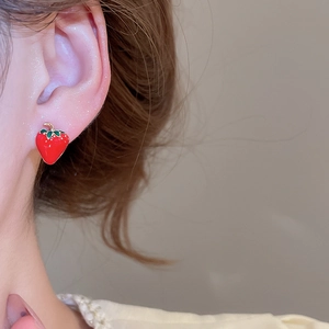 Close-up of a vibrant red strawberry stud earring with green leaves worn on a woman's ear