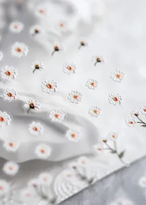 Macro shot of 3D white daisy nail art stickers with delicate yellow centers on lace
