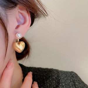 Close-up of model wearing gold heart earrings with pearl accents and brushed metal texture