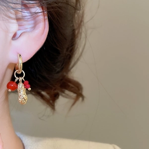 Macro shot of gold peanut pendant earrings with red crystal beads on a female model