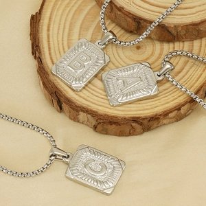 Macro shot of silver square pendant necklaces with embossed letters A, B, and C on wood