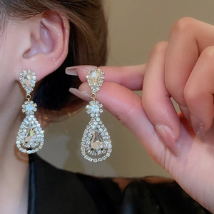 Macro view of crystal teardrop tassel earrings with silver needles worn by model