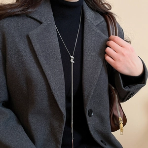 Detail of silver long sweater necklace with H-pendant on black turtleneck sweater