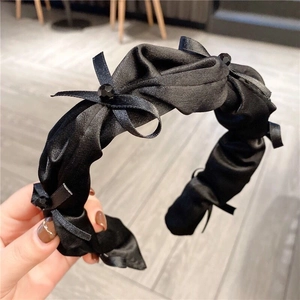 Detail of a pleated black satin headband featuring elegant knotted design and small beads
