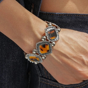 Detailed shot of retro geometric acrylic bracelet with vintage metallic carvings on denim