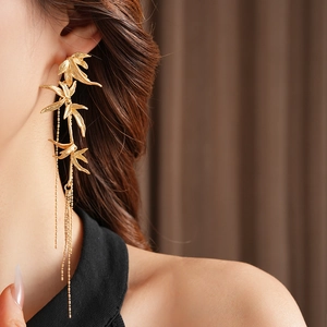 Close-up of elegant gold bamboo leaf earrings with long tassels on female model
