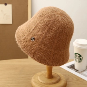 Japanese style camel knit bucket hat with metal emblem on a wooden stand in a cozy setting