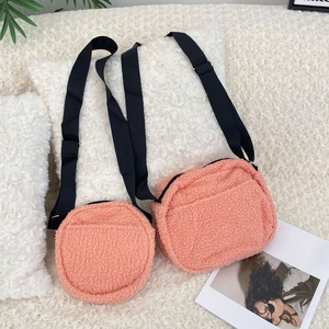 Detail of pink faux shearling crossbody bags with adjustable black straps on plush background
