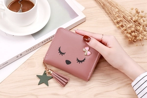 Pink cartoon tassel wallet with eyelash design on wooden table with coffee cup