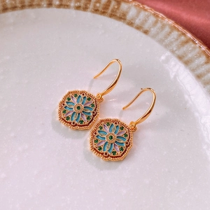 Detailed close-up of vintage gold earrings with colorful enamel floral patterns in a ceramic tray