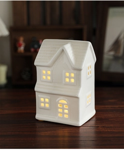 Detail of white ceramic Christmas house ornament with warm LED light on wooden table