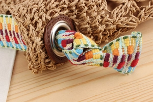 Close-up of woven straw bag detail featuring colorful geometric strap and silver eyelet