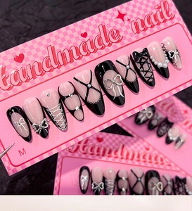 Detail of handmade almond press-on nails featuring black bows, pearls and corset design