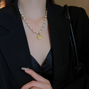 Nahaufnahme eines goldenen Münzanhängers mit Perlenhalskette an einem Model in Schwarz