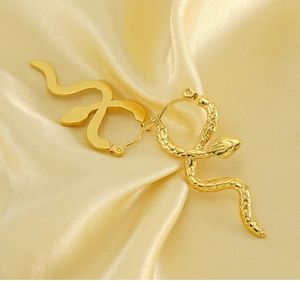 Close-up of golden snake drop earrings with smooth and scaled textures on silk fabric