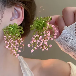 Handmade beaded flower tassel earrings with green and pink beads on female model