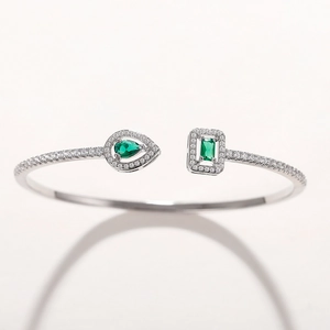 Detail view of a silver open bangle featuring pear-cut green gems and micro-set cubic zirconia