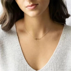Detail of a minimalist horizontal gold cross pendant on a delicate cable chain necklace