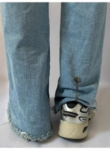 Detail of light blue frayed denim hem with metal chain and button fastener