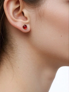 Close-up of model wearing gold-rimmed red jade studs in a minimalist round design