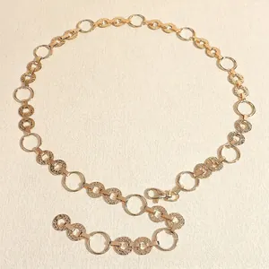 Detail of gold metal waist chain belt with embossed rings and adjustable lobster clasp