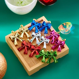 Colorful geometric Christmas bow earrings in six metallic colors on a festive wooden tray