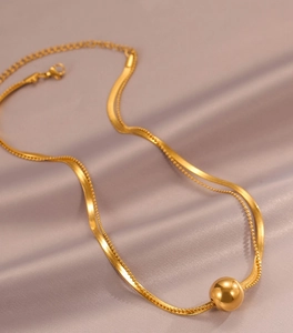 Detail of double-layer gold snake and bead chain necklace with polished sphere pendant