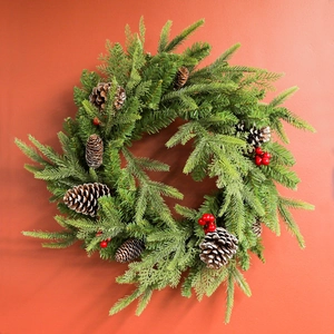 Christmas wreath with snowy pine needles, pine cones and red berries on a rustic background